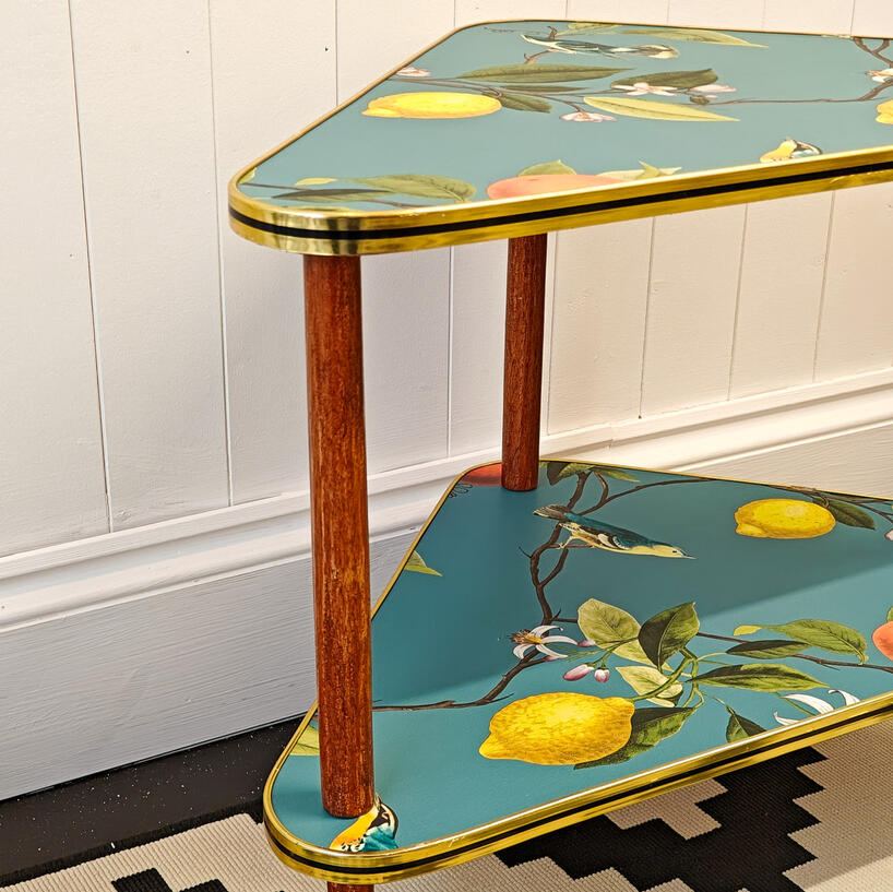 An upcycled mid-century modern corner side table with restored wooden legs, a gorgeous flora and fauna print, retaining the original gold and black trim.